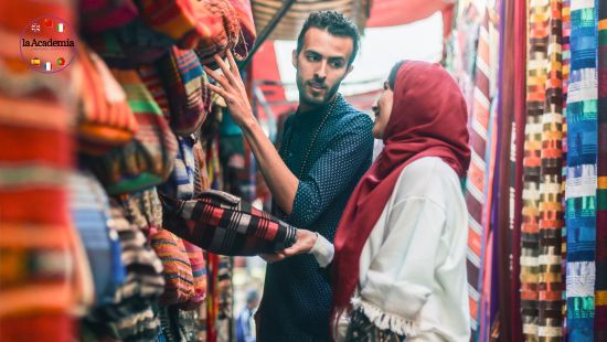 An Asian man and a woman in a hijab haggling over the price of textile rolls at a market.