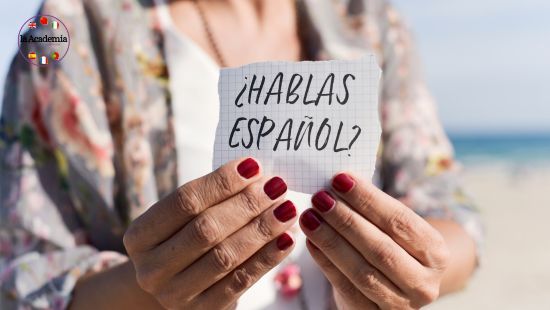 A pair of woman's hand with burgundy painted fingernails holding a sign saying Hablas Espanol?