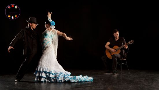A flamenco couple in traditional dress dancing to a Spanish guitarist